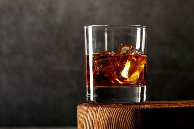 A glass of whiskey on the rosks in front of a dark gray background