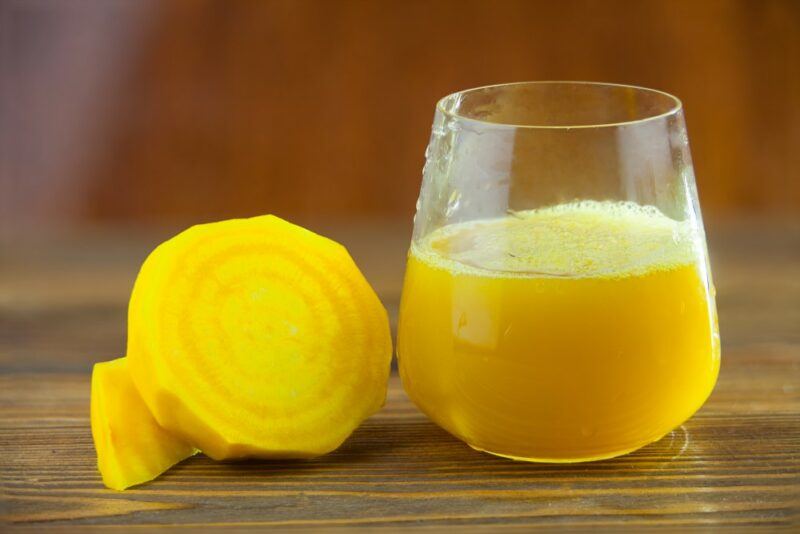 A glass of yellow beet juice, next to half a yellow beet