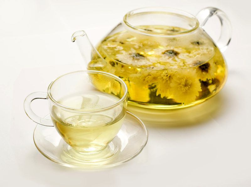 A glass jug of chrysanthemum tea that contains many flowers, along with a glass cup of the tea