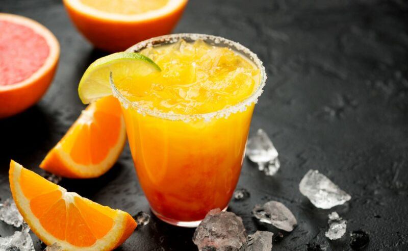 A glass of an orange margarita next to oranges