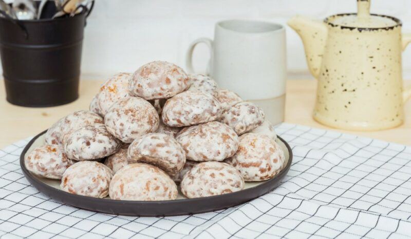 A checkered cloth with a plate of stacked pryaniki cookies, with a mug and jug in the background