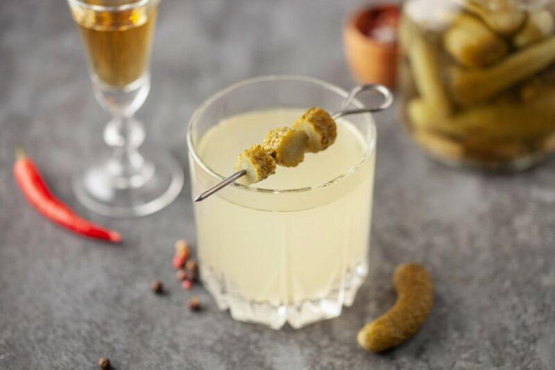 A gray table with a pickle juice cocktail and a glass of some spirit in the background