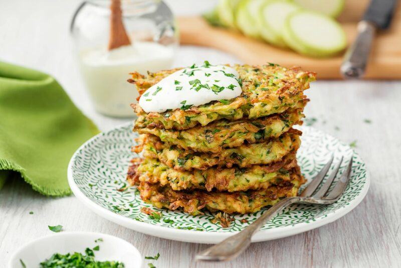 A dish with a stack of zucchini fritters with sour cream