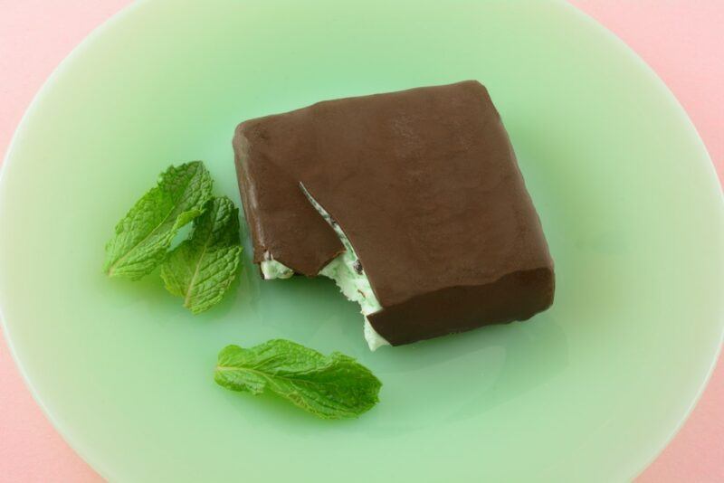 A light green plate with a square containing a peppermint ice cream bite and three mint leaves