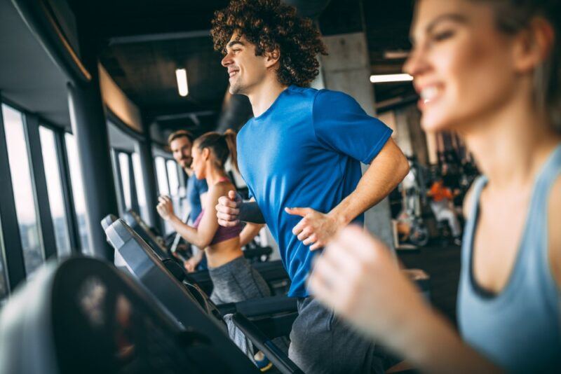 A group of men and women in a gym running on treadmills