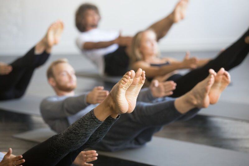 A group of people on gray mats practicing yoga with their legs in the air