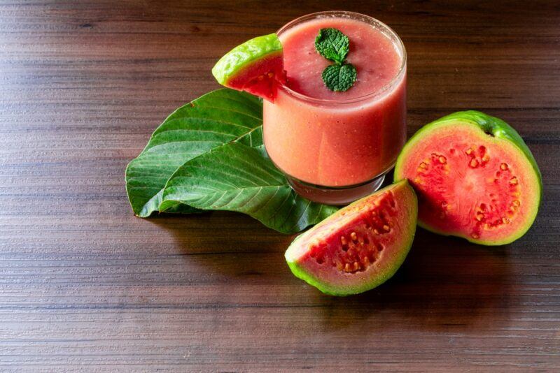 A glass of fresh guava smoothie, next to a guava and a guava wedge