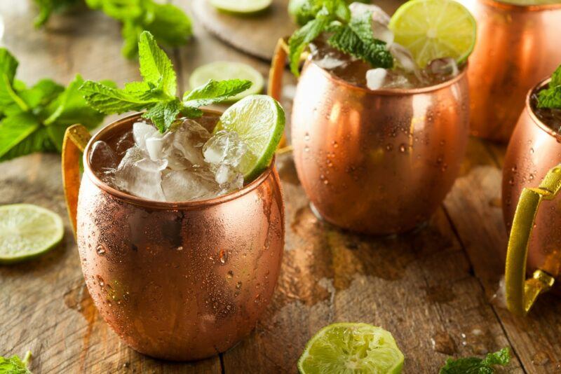 A wooden table with various copper mugs containing a Shanghai mule cocktail, plus pieces of lime and peppermint leaves