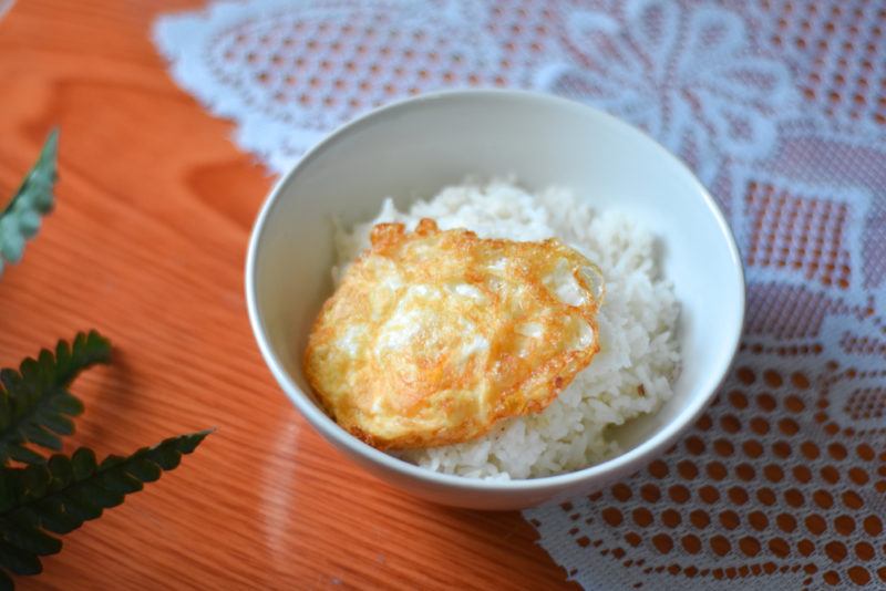 A hard fried egg being served over rice in a bowl