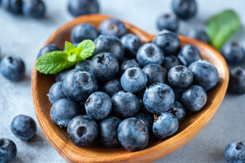 A wooden bowl shaped like a heart and filled with blueberries