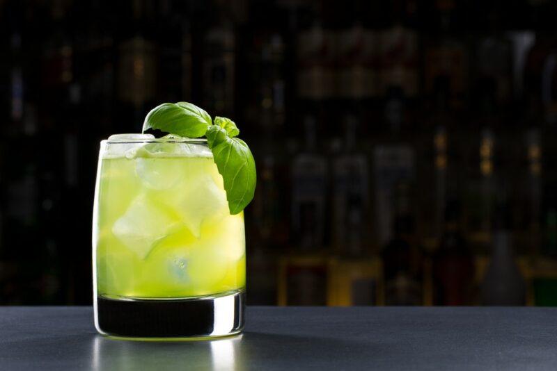 A dark table containing a light green honey dew cocktail with a darkened bar in the background