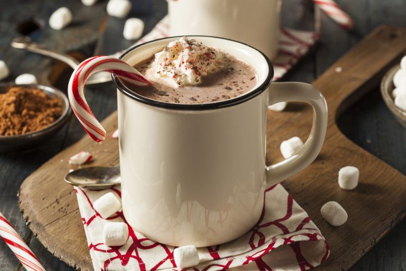 A ceramic mug of hot chocolate with a candy cane sticking out of it and marshmallows scattered around