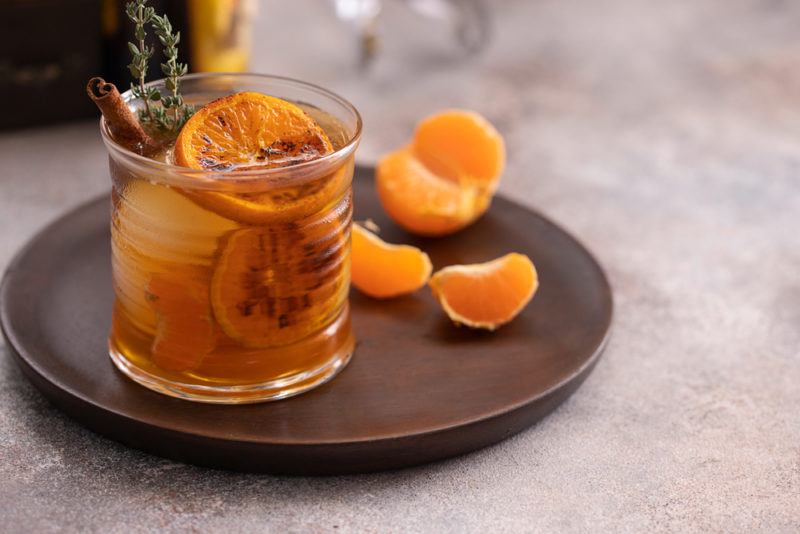 A wooden tray with a hot cocktail in a glass, with fruit and cinnamon as a garnish