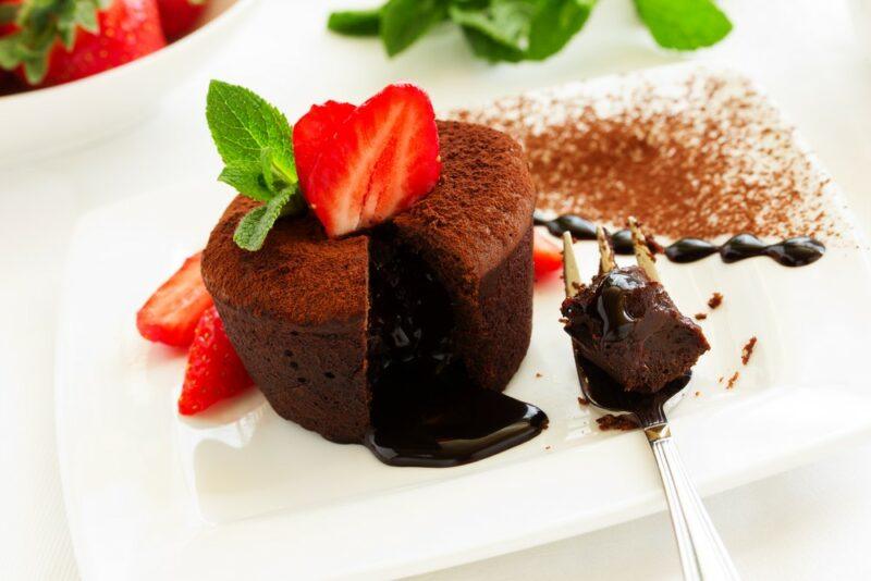 A white tray with a chocolate lava cake, with strawberries on top. A fork has been used to break into the cake