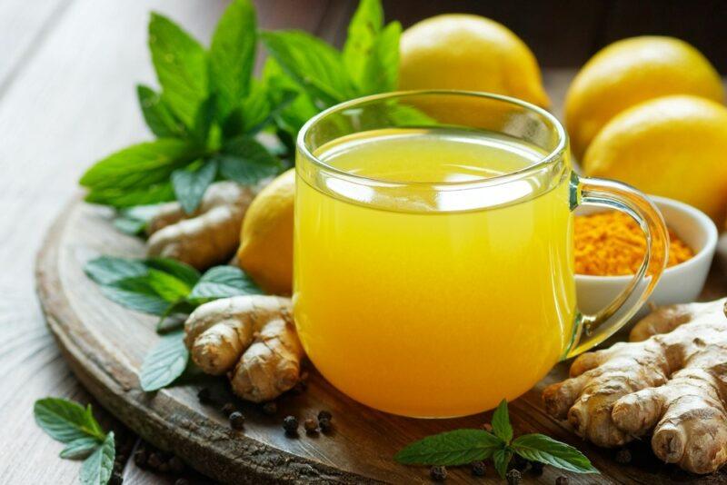 A glass mug filled with hot lemon tonic on a board, with lemons and spices nearby