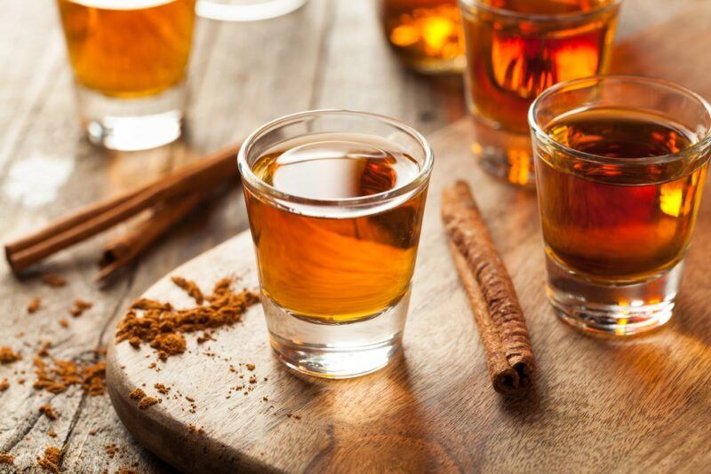 A wooden board with shot glasses that all contain a hot little honey shot, with cinnamon sticks on the table