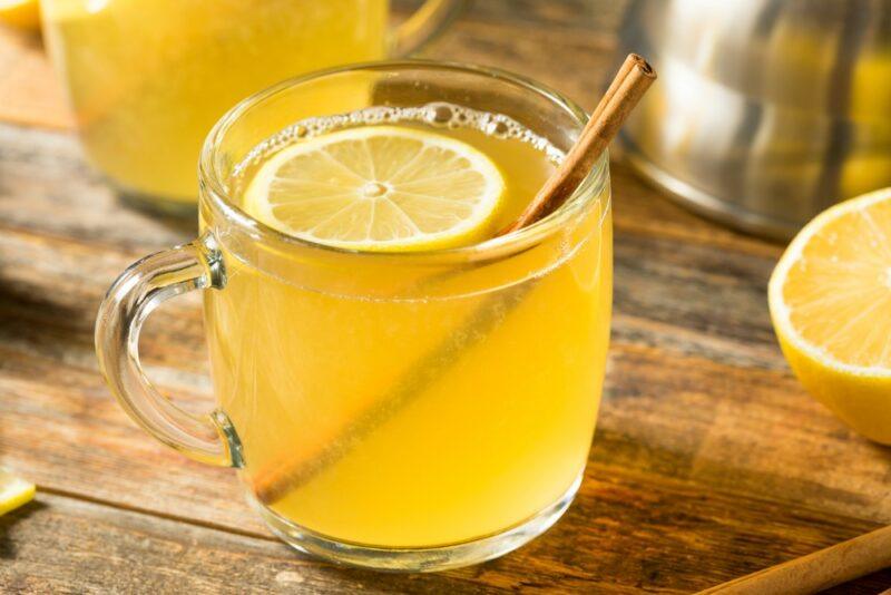 A wooden table with two mugs containing a hot toddy, with a slice of lemon and a cinnamon stick