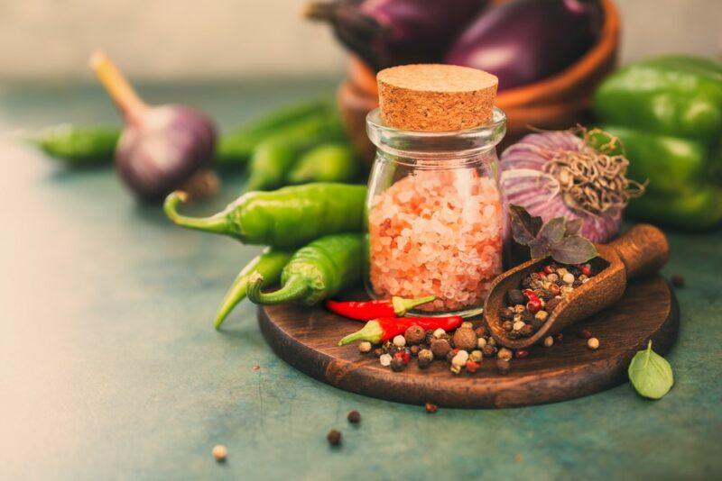 A flat tray containing a jar of Himalayan salt, next to peppercorns, fresh peppers, and other ingredients