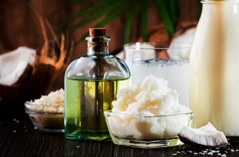 A jar of MCT oil near some coconut oil with coconuts in the background