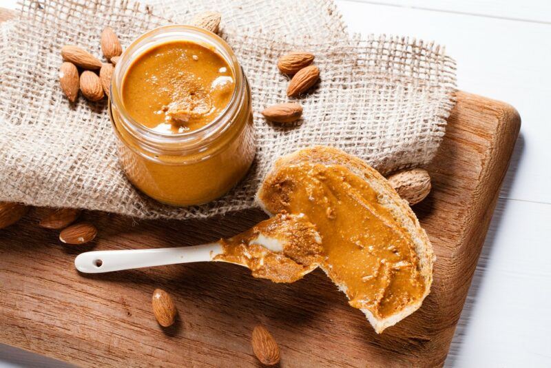 A jar of almond butter, next to a spoon of the butter, and almond butter spread on toast