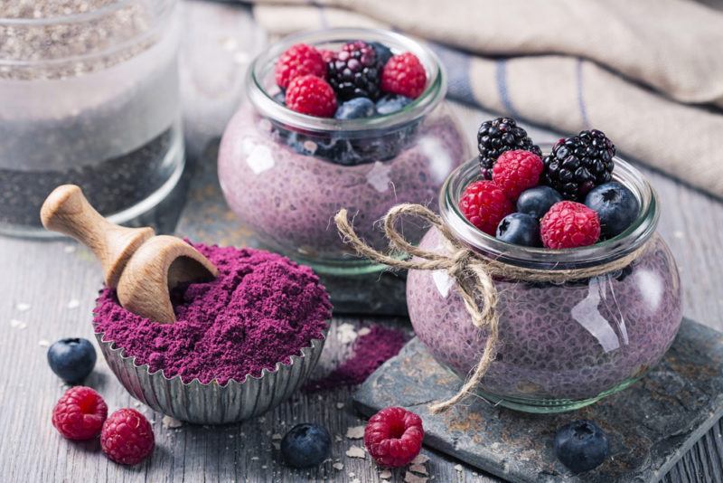 Two glass jars of chia seed pudding, topped with berries, and a container of acai powder with a scoop