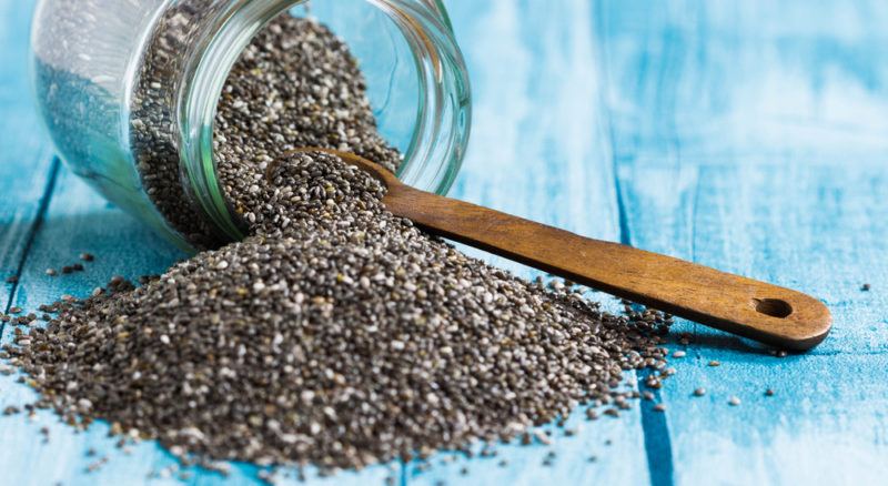 A jar of chia seeds with a spoon, where the chia seeds are spilling out onto the table