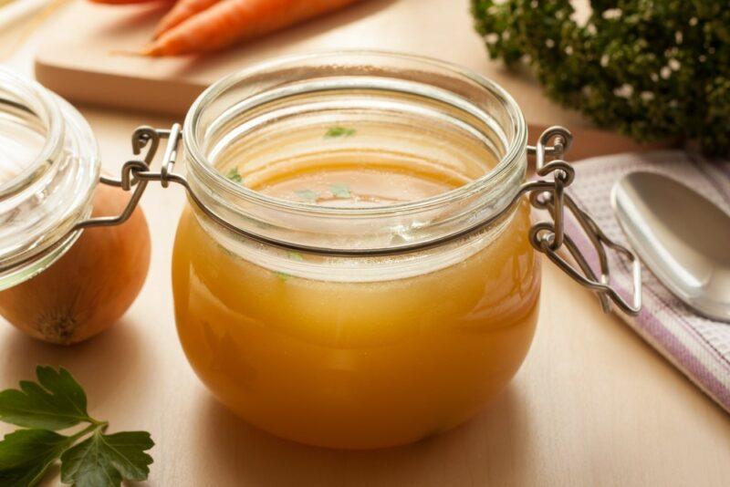 A glass jar filled with chicken broth with carrots and other ingredients in the background