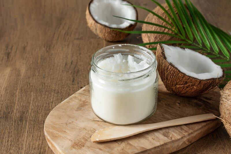 A jar of coconut oil next to two coconut halves