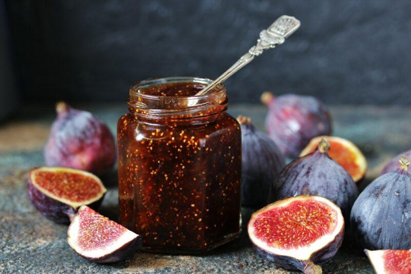 A jar of fig jam with a spoon, with fresh figs and fig halves on a table