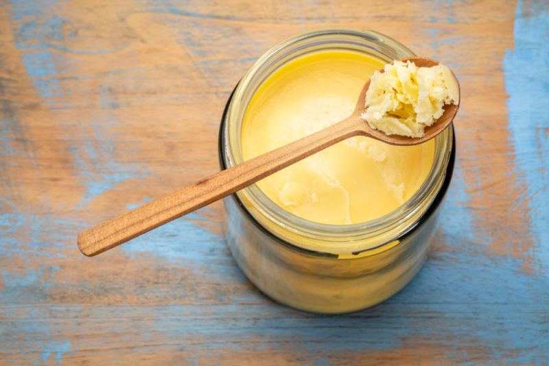 A glass jar of ghee with a wooden spoon