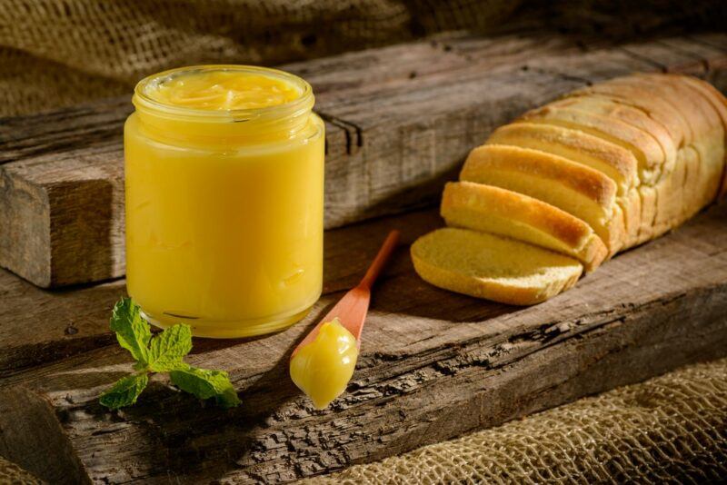 A glass jar of ghee next to some sliced bread