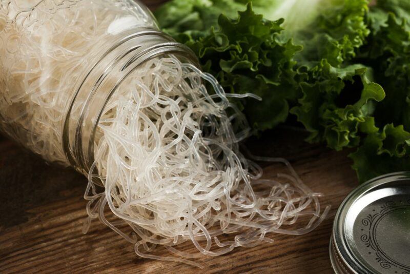 A jar of white kelp noodles spilling onto a wooden table, next to seaweed