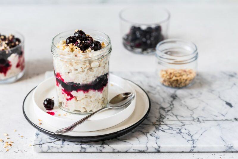 A marble tray with overnight oats and a spoon. There's a smaller container of oats in the background, along with some blueberries and another of overnight oats