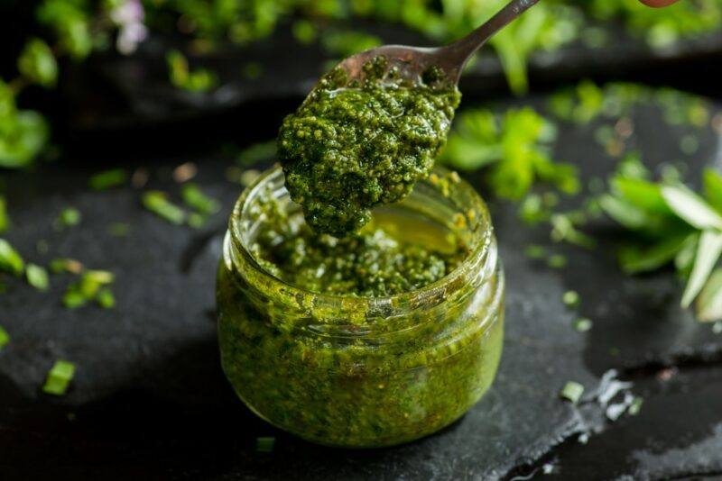 A black table containing a jar of pesto, where some is being scooped out with a spoon