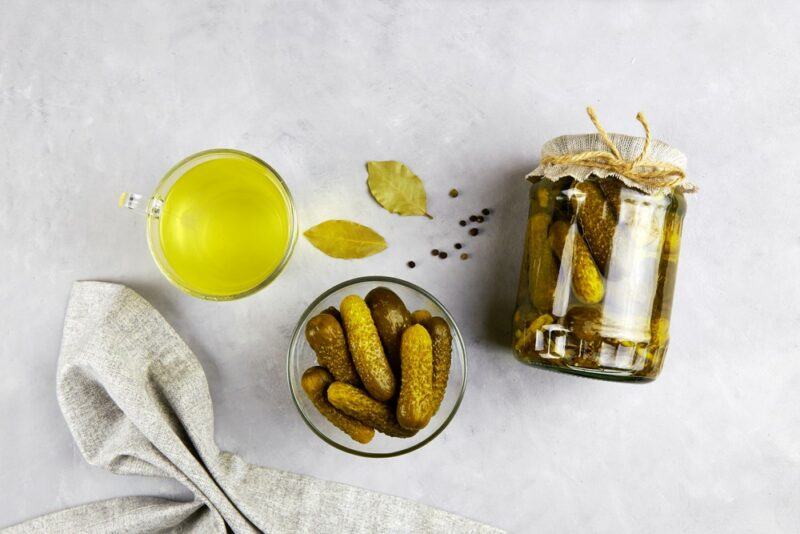 A jar of pickles, with a small dish of them and some pickle juice