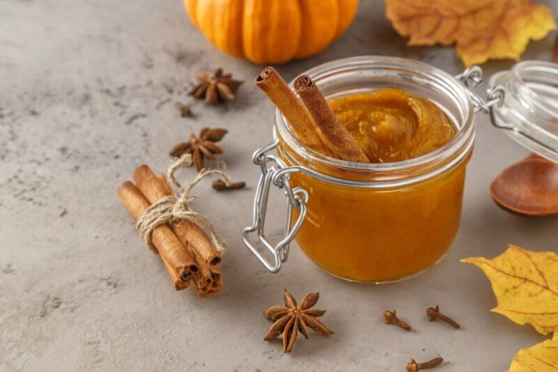 A glass jar of spiced butter next to spices and some pumpkins