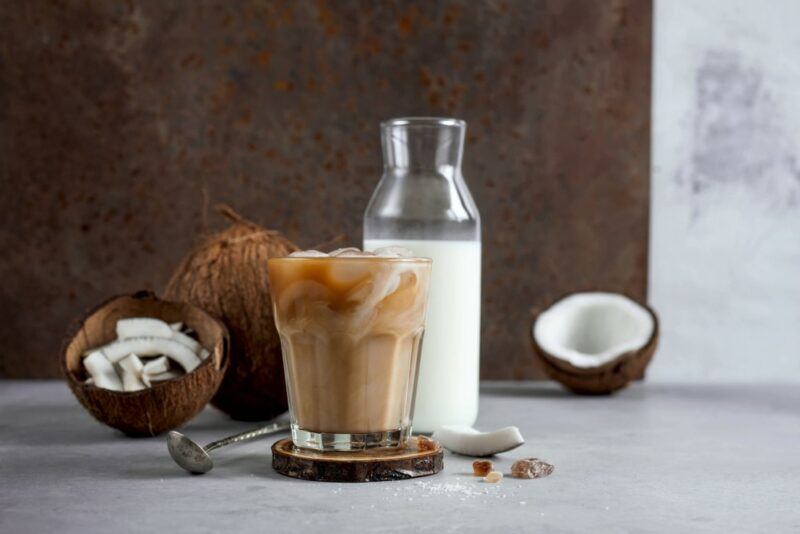 A bottle of coconut milk next to a coffee made with the milk and some coconuts