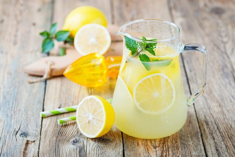 A glass jug of homemade lemonade on a wooden table, next to some lemon halves