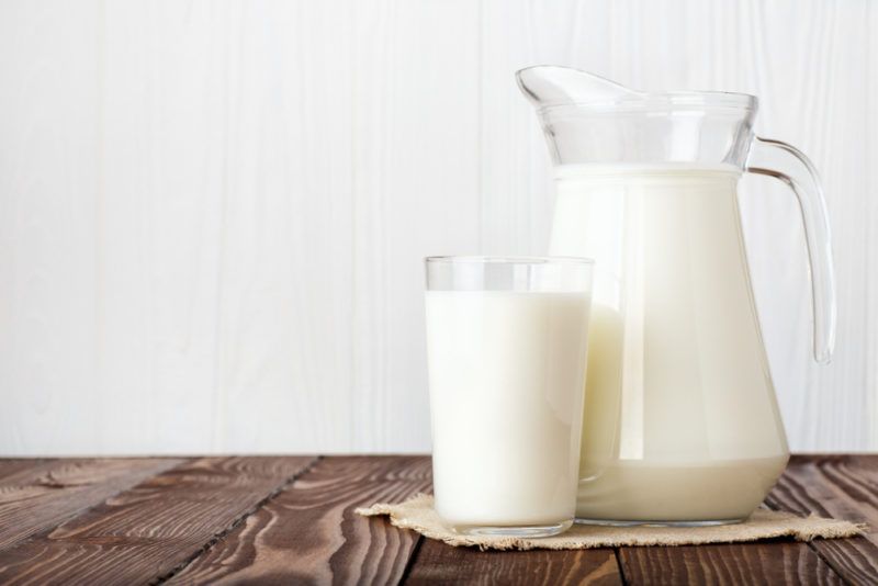 A jug of milk and a glass of milk on a wooden table