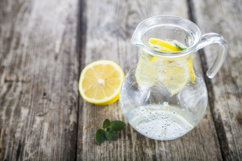 A wooden table with a jug of tonic water and lemons. There's a single lemon half on the table as well