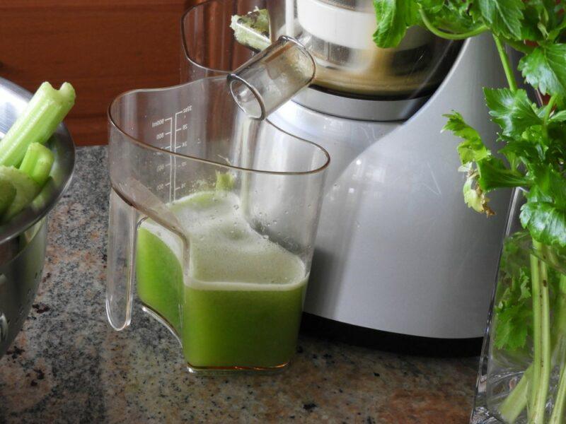 A close up image of a white juicer, with celery juice collecting in a container