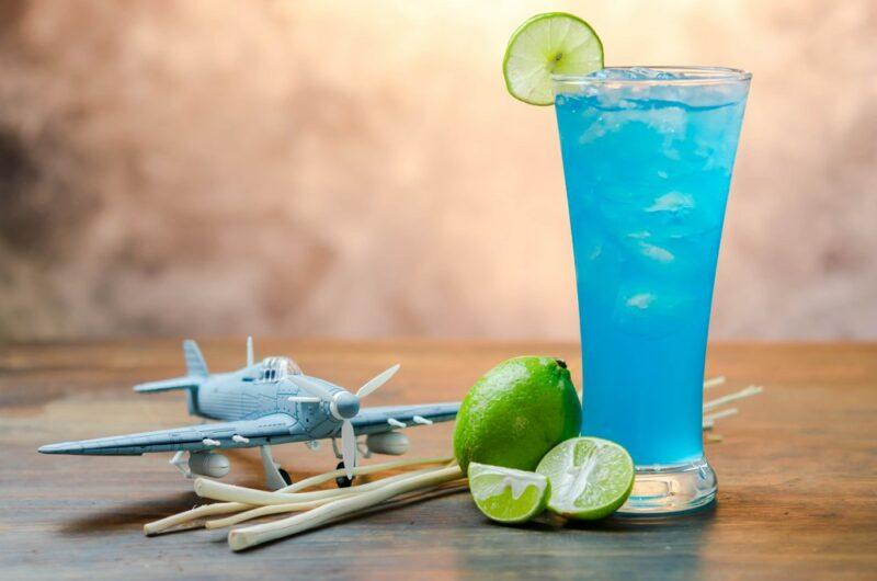 A tall glass containing a kamikaze cocktail , next to a plastic plane, some limes, and some toothpicks