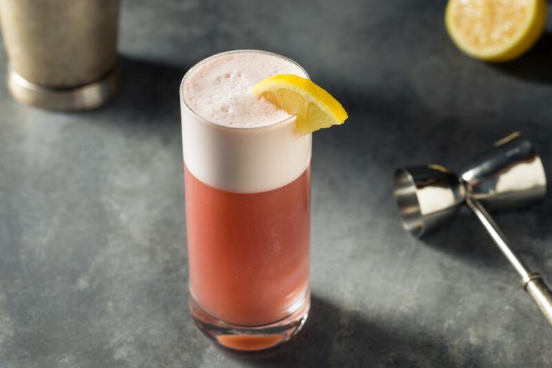 A tall glass containing a kiss of sake cocktail with a fizz top, next to a cocktail jigger