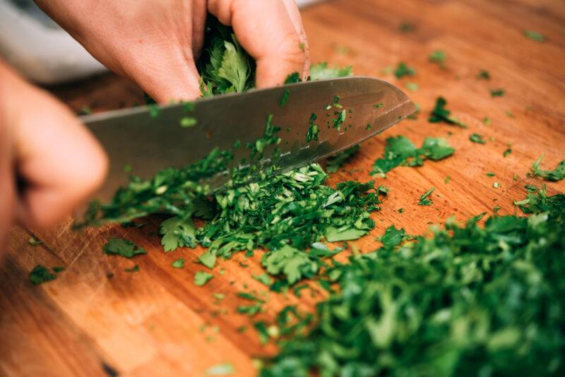 A kitchen knife being used to chop herbs on a cutting board, highlighting some of the best kitchen knife brands