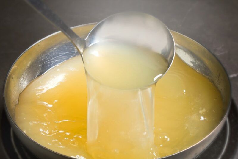 A steel pot filled with chicken broth, with some being taken out using a ladel