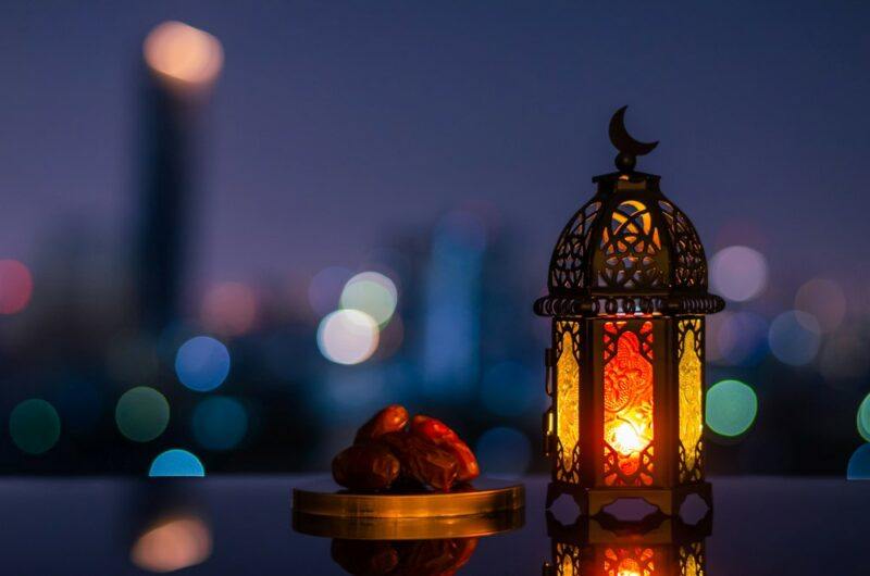 The dimmed out lights of a city with a lamp and dates in the foreground, as an indication of Ramadan