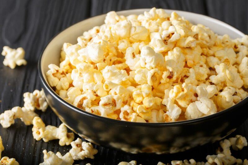 A black bowl with parmesan and garlic popcorn, with some pieces of popcorn on the table