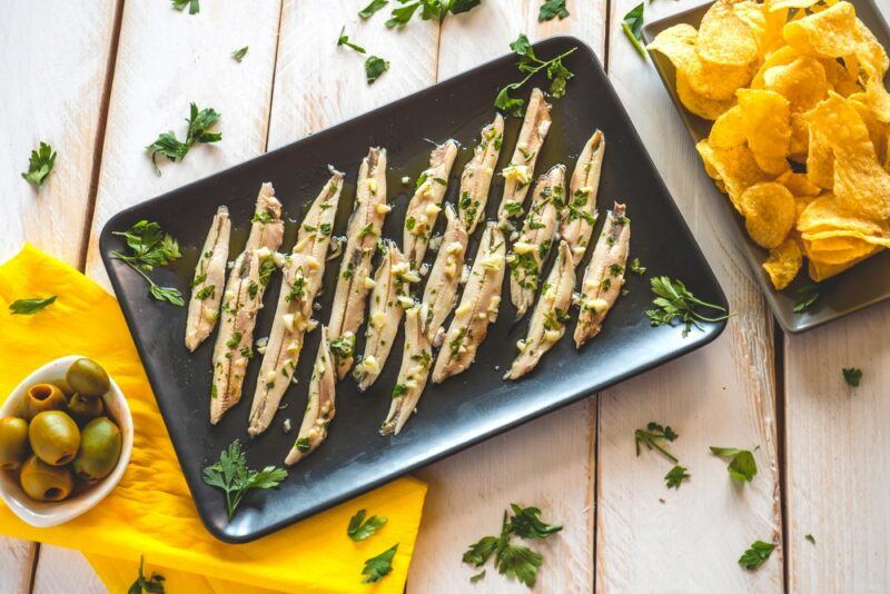 A rectangular dish of cooked anchovies on a wooden table