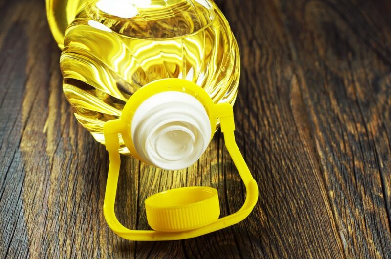 A wooden table with a large bottle of canola oil, with a yellow cap