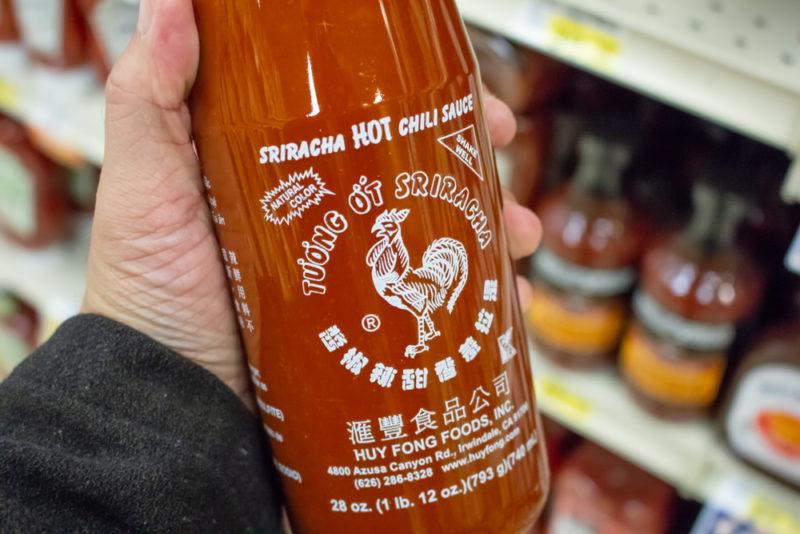 A large bottle of sriracha being held in a grocery store